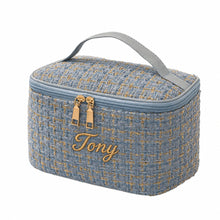 Carica l'immagine nel visualizzatore di Gallery, A rectangular zippered toiletry or vanity bag in textured blue tweed with gold-toned woven accents, a gray top handle, and gold-tone zipper pulls, shown on a plain white background.
