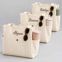 Carica l'immagine nel visualizzatore di Gallery, Three cream canvas tote bags with personalized names (Alyssa, Brianna, Katelyn) in dark brown script, styled with sunglasses and tumblers in a bright, sunlit room.
