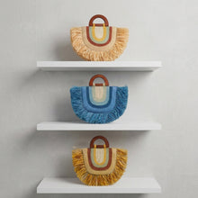 Load image into Gallery viewer, A display of handmade fringe handbags hanging on a rack in a shop. The bags feature a retro arch design with fringe trim, wooden handles, and colorful striped accents in blue, yellow, orange, and green.
