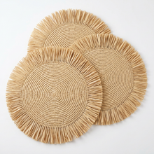 Cargar imagen en el visor de la galería, Natural woven round placemats with frayed fringe edges, shown overlapping on a light surface. The photo appears to be a screenshot from a phone app, with a dark interface and a row of thumbnail previews along the bottom.
