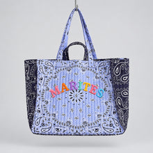 Load image into Gallery viewer, A quilted tote bag with a light blue paisley bandana pattern, featuring colorful embroidered text reading 'MARITES' on the front, hanging from a wooden cloud-shaped peg on a plain off-white wall.
