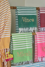 Carica l'immagine nel visualizzatore di Gallery, Personalized beach towel with custom name embroidery hanging among other striped towels
