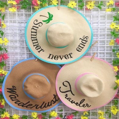 Three custom hand-painted floppy hats with colorful brims and travel-themed text hanging on a floral backdrop